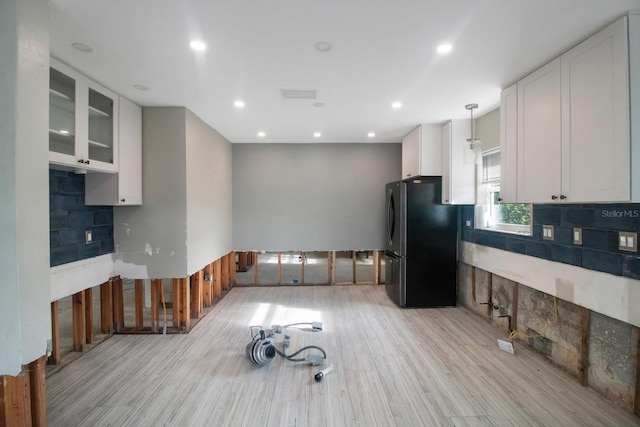 kitchen with white cabinets, pendant lighting, light hardwood / wood-style floors, and black fridge