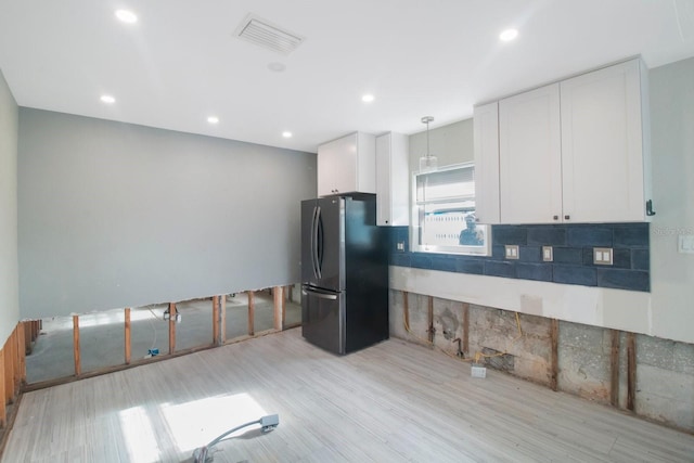 kitchen with black refrigerator, white cabinets, pendant lighting, and light hardwood / wood-style floors