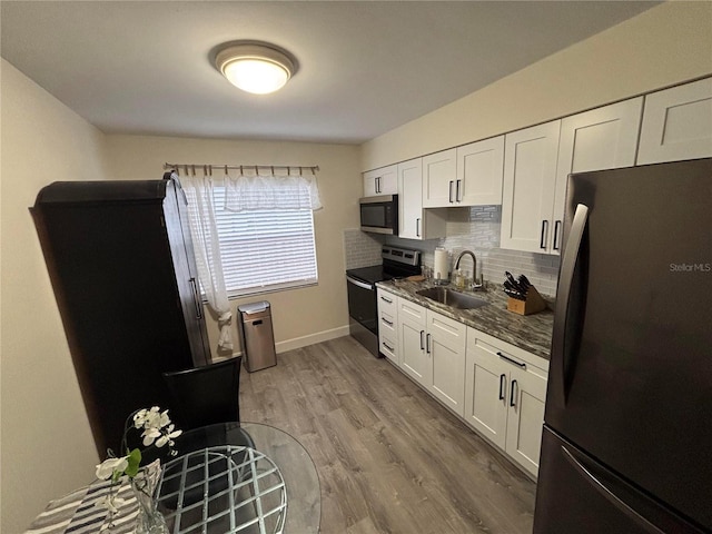 kitchen with white cabinets, stainless steel appliances, dark stone counters, and sink