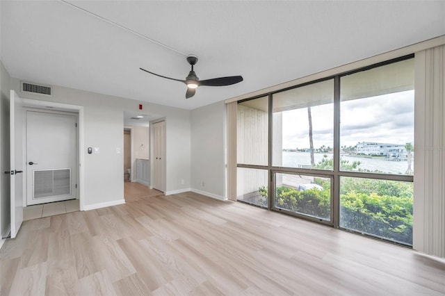 empty room featuring a water view, light hardwood / wood-style flooring, expansive windows, and ceiling fan