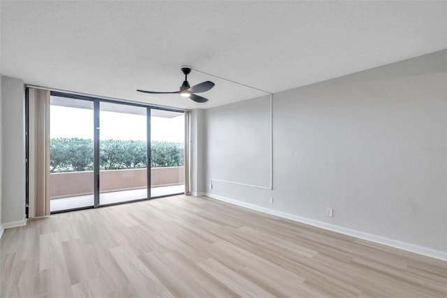 spare room featuring light wood-type flooring, a textured ceiling, a wall of windows, and ceiling fan