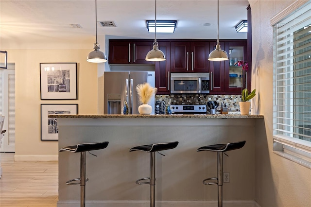 kitchen featuring decorative backsplash, pendant lighting, appliances with stainless steel finishes, and a breakfast bar area