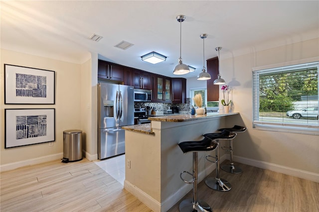 kitchen with decorative light fixtures, kitchen peninsula, appliances with stainless steel finishes, and light wood-type flooring