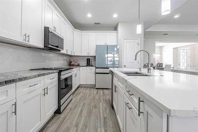 kitchen with backsplash, white cabinetry, stainless steel appliances, and a kitchen island with sink