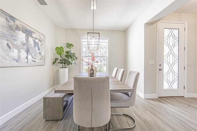 dining space featuring light hardwood / wood-style floors, a textured ceiling, and a notable chandelier