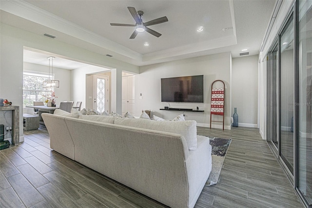 living room with a tray ceiling, ceiling fan with notable chandelier, and ornamental molding