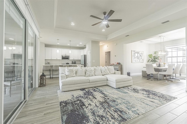 living room featuring ceiling fan with notable chandelier, a raised ceiling, and ornamental molding