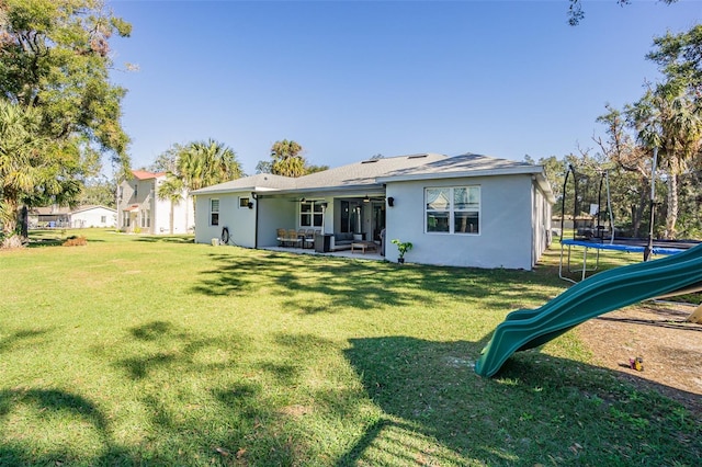 rear view of property featuring a lawn, ceiling fan, a trampoline, a playground, and a patio