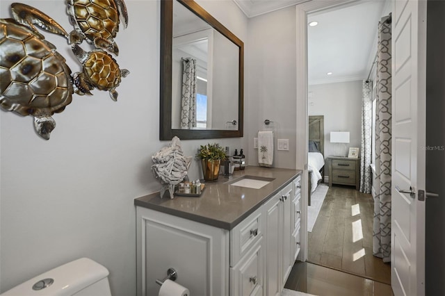 bathroom with toilet, ornamental molding, wood finished floors, recessed lighting, and vanity