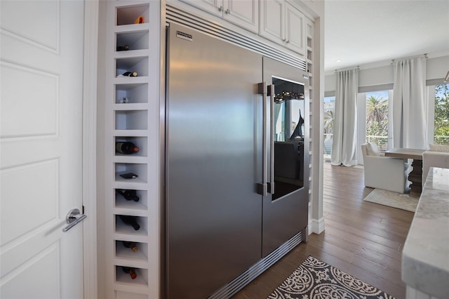 kitchen with dark wood-type flooring, stainless steel built in refrigerator, and white cabinetry