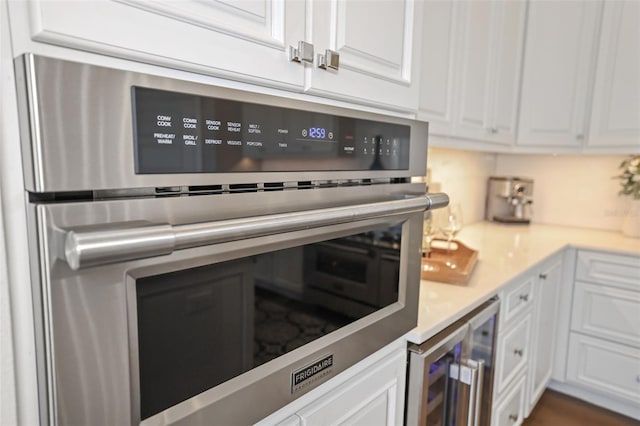 kitchen with wine cooler, white cabinets, light countertops, and stainless steel oven