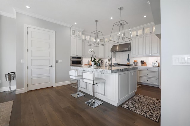 kitchen with crown molding, under cabinet range hood, stainless steel oven, dark wood-style floors, and white cabinetry