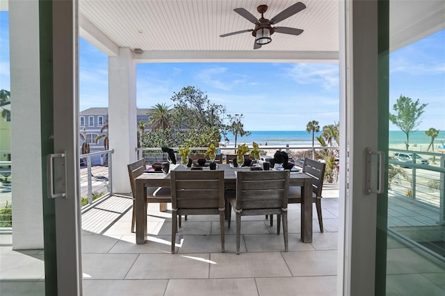 balcony with a beach view, outdoor dining area, a ceiling fan, and a water view