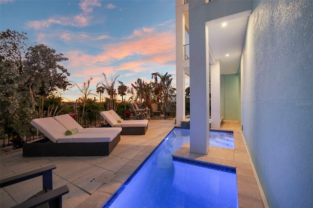 pool at dusk with an outdoor pool and a patio