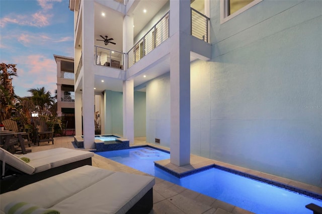 pool at dusk featuring a patio area, a pool with connected hot tub, and a ceiling fan