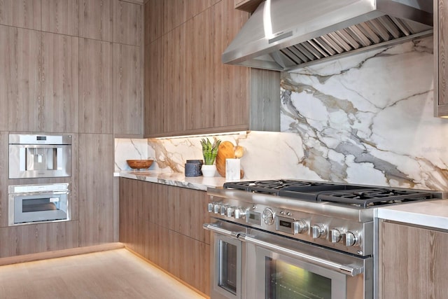 kitchen with backsplash, light hardwood / wood-style floors, wall chimney exhaust hood, and appliances with stainless steel finishes