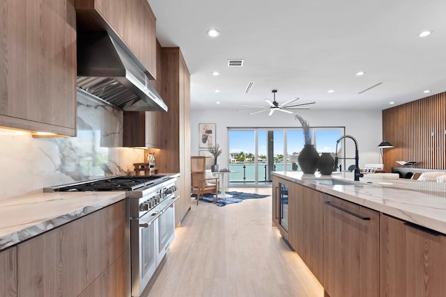 kitchen with light stone counters, sink, range with two ovens, and wall chimney range hood