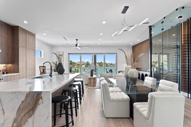 dining area with sink, light wood-type flooring, ceiling fan, and a water view