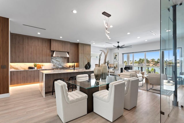 dining space with ceiling fan, a water view, sink, and light hardwood / wood-style floors