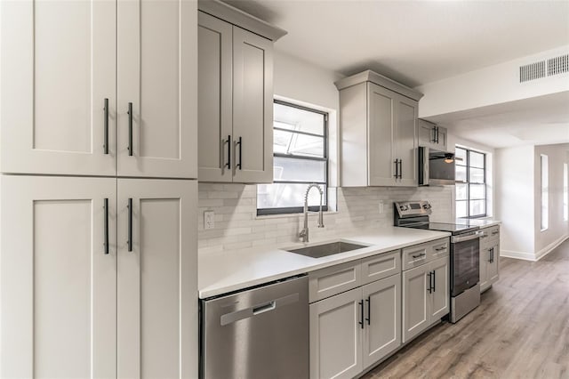 kitchen featuring gray cabinetry, a sink, visible vents, appliances with stainless steel finishes, and decorative backsplash