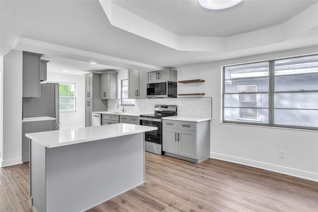 kitchen featuring gray cabinetry, tasteful backsplash, light wood-type flooring, appliances with stainless steel finishes, and a tray ceiling