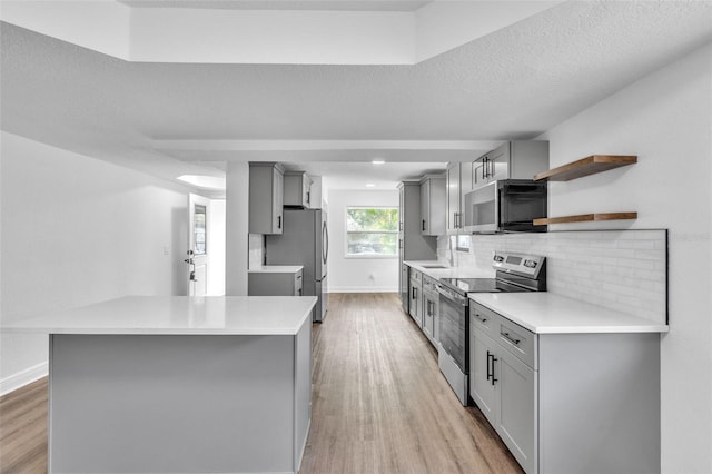 kitchen with appliances with stainless steel finishes, light wood-type flooring, gray cabinetry, and a textured ceiling