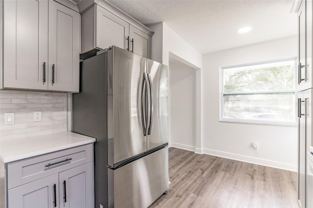 kitchen featuring gray cabinets, stainless steel refrigerator, light hardwood / wood-style floors, a textured ceiling, and decorative backsplash