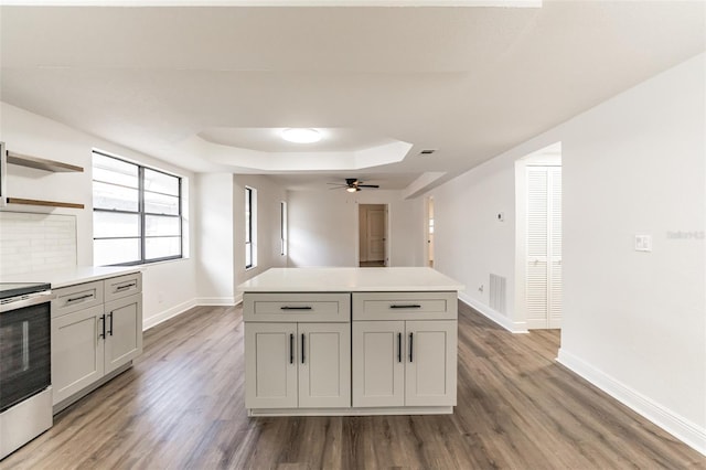 kitchen with wood-type flooring, a center island, stainless steel electric range, a raised ceiling, and ceiling fan