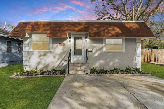 view of front of property featuring a shingled roof, mansard roof, and stucco siding