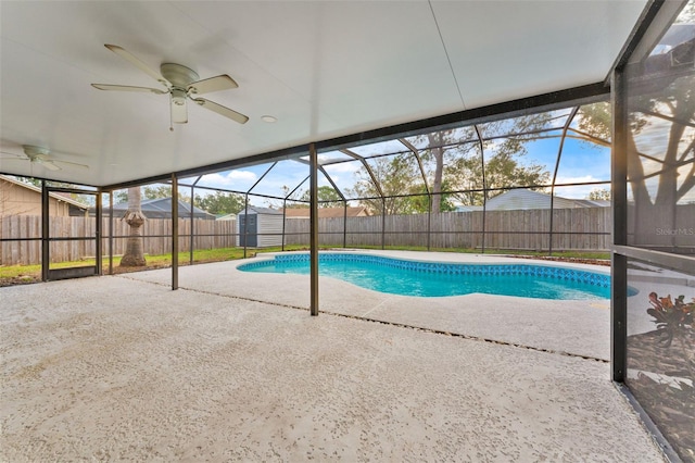 view of pool featuring ceiling fan, a patio area, a shed, and glass enclosure