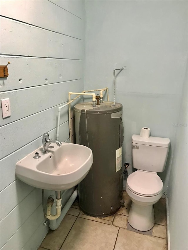 bathroom with electric water heater, sink, wood walls, and toilet