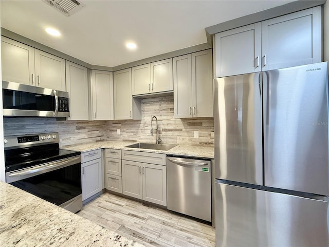 kitchen with gray cabinetry, appliances with stainless steel finishes, sink, and light stone counters