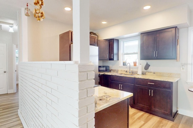 kitchen with light stone counters, dark brown cabinetry, sink, white fridge, and light hardwood / wood-style floors