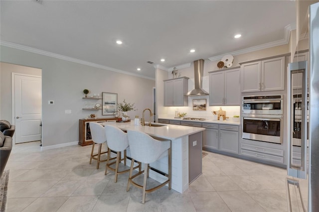 kitchen featuring a kitchen bar, gray cabinets, stainless steel appliances, and wall chimney range hood