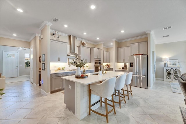 kitchen featuring gray cabinets, wall chimney range hood, stainless steel appliances, and a kitchen island with sink