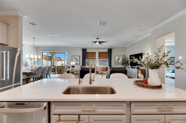 kitchen with appliances with stainless steel finishes, ceiling fan with notable chandelier, sink, white cabinetry, and an island with sink