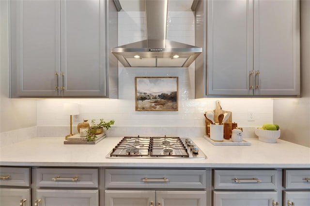 kitchen featuring backsplash, gray cabinets, stainless steel gas stovetop, and wall chimney range hood