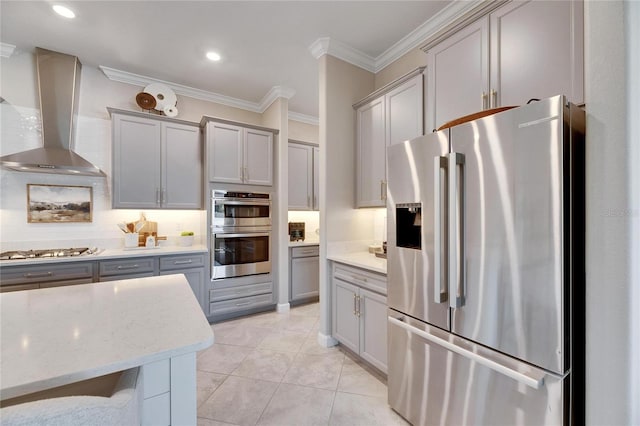 kitchen featuring wall chimney range hood, crown molding, gray cabinets, light tile patterned flooring, and appliances with stainless steel finishes