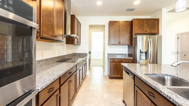 kitchen featuring light stone countertops, stainless steel appliances, wall chimney exhaust hood, and sink