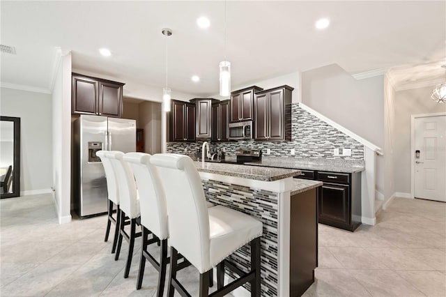 kitchen with crown molding, light stone countertops, an island with sink, appliances with stainless steel finishes, and decorative light fixtures