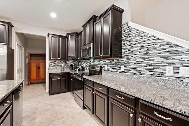 kitchen with light stone countertops, appliances with stainless steel finishes, backsplash, dark brown cabinets, and light tile patterned floors