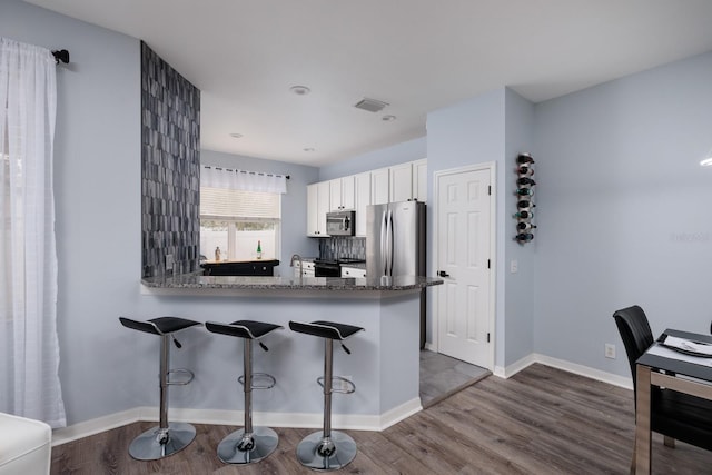 kitchen with backsplash, dark stone countertops, white cabinetry, kitchen peninsula, and stainless steel appliances