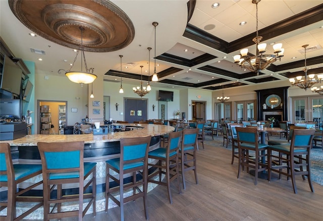 kitchen featuring hardwood / wood-style flooring, light stone countertops, decorative light fixtures, a large island with sink, and coffered ceiling