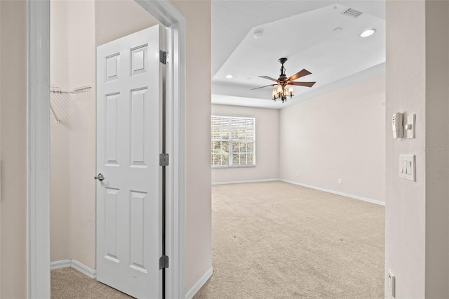 corridor with light colored carpet and a raised ceiling