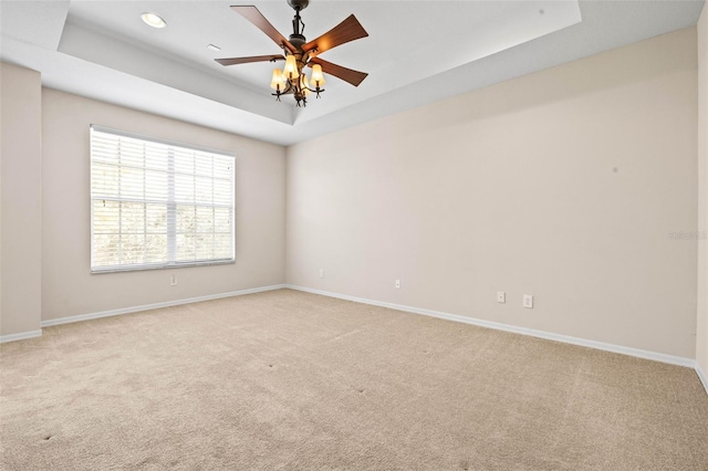 empty room with ceiling fan, a raised ceiling, and light carpet