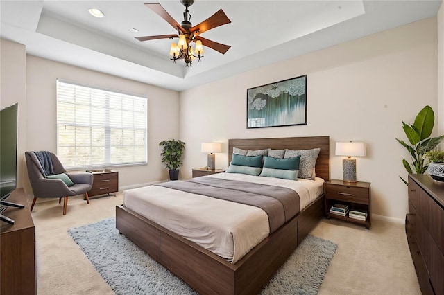 bedroom with light colored carpet, a raised ceiling, and ceiling fan