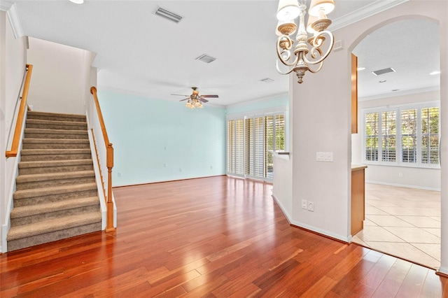 empty room with wood-type flooring, ceiling fan with notable chandelier, and crown molding