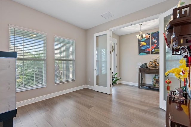 interior space featuring light wood-type flooring, french doors, and a notable chandelier