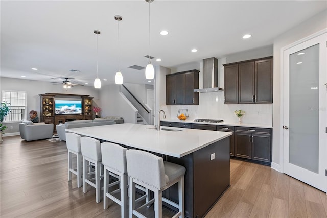 kitchen featuring ceiling fan, wall chimney range hood, pendant lighting, a breakfast bar, and sink