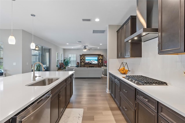 kitchen featuring wall chimney range hood, stainless steel appliances, tasteful backsplash, sink, and hanging light fixtures